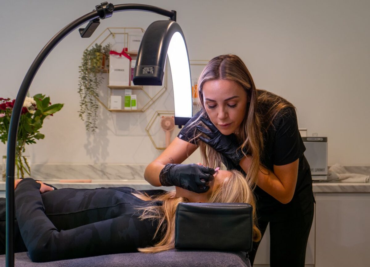 Beauty technician applying eyelash extensions to a client in a modern salon setting.