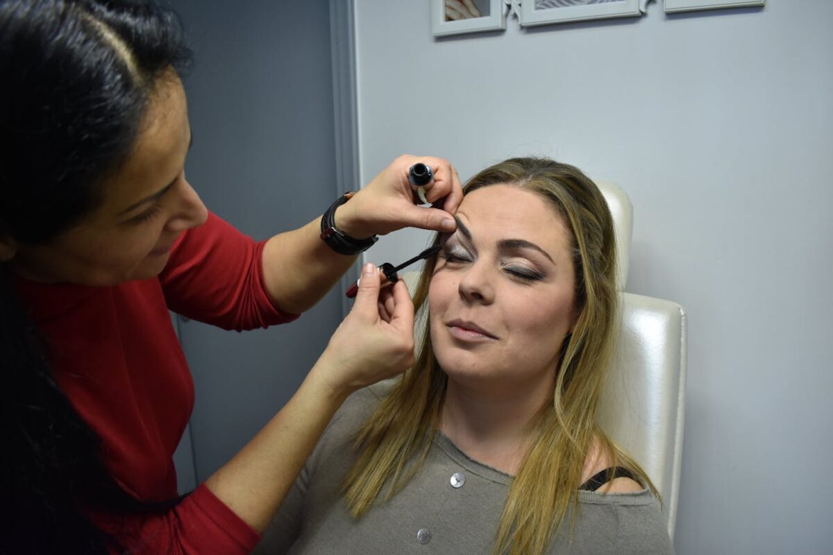 Makeup artist applies mascara to a woman indoors, highlighting beauty and care.